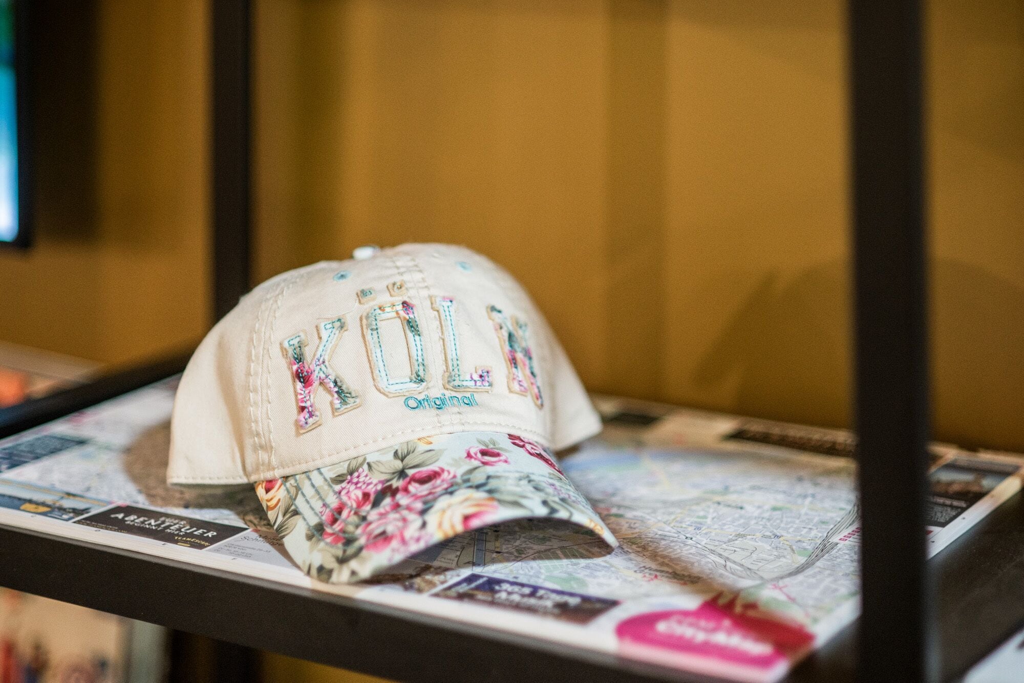 A cap with embroidered text and floral design on a display stand.