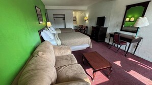 Une chambre d’hôtel avec un mur vert, un lit avec deux oreillers, un canapé, un bureau avec une chaise et un téléviseur.