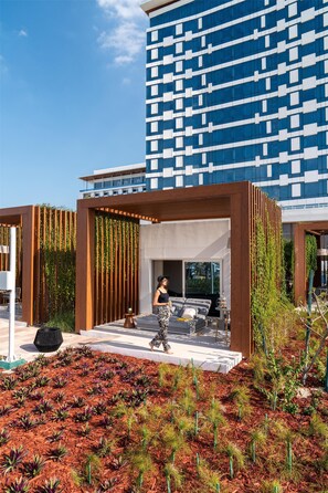 A modern outdoor area with a seating area, a pergola with climbing plants, and a view of a high-rise building.