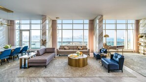 A spacious living room with a large window offering a city view, a sofa, a coffee table, and a dining area with chairs.