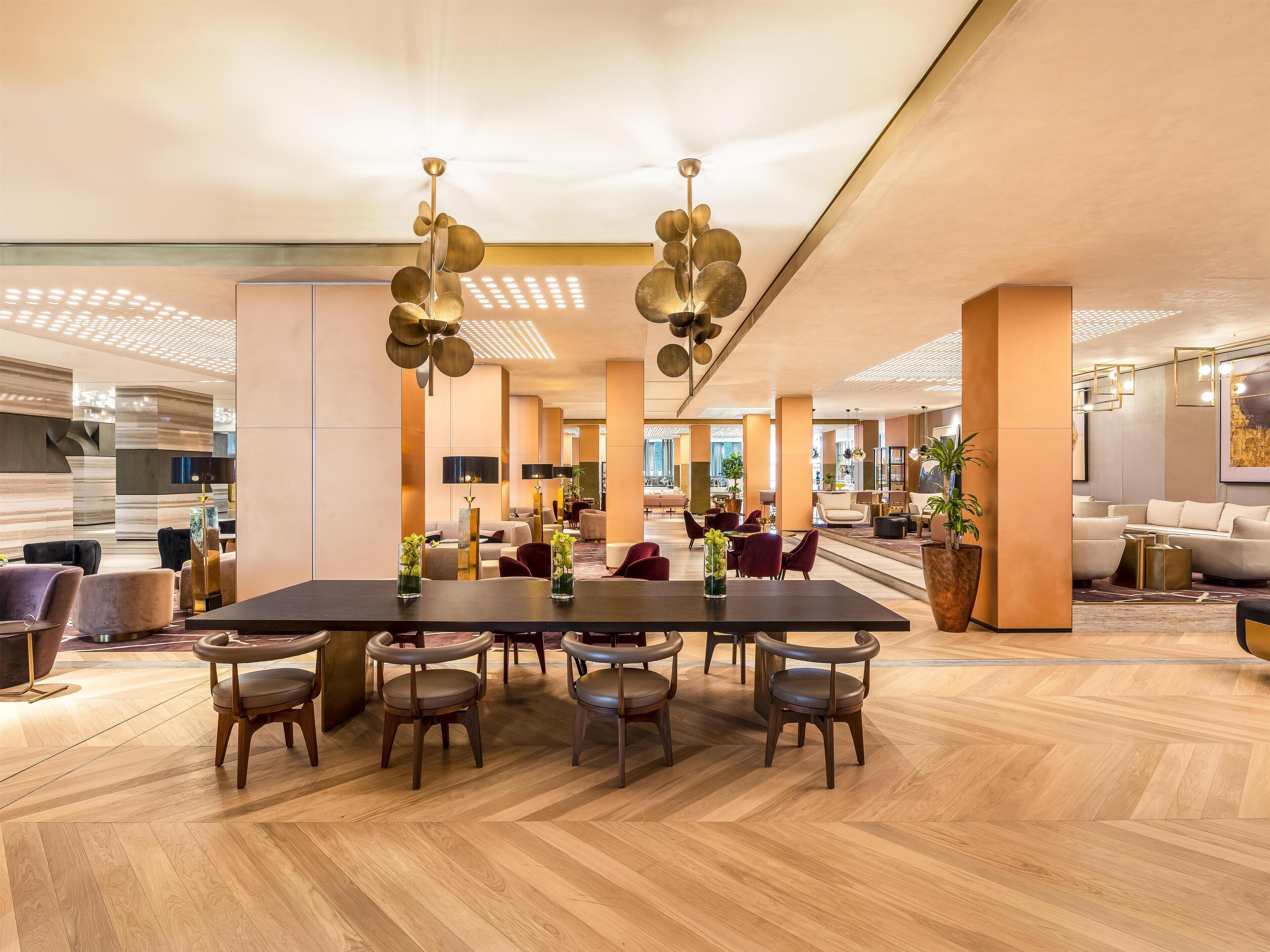 A spacious lobby with a large wooden table, comfortable seating, and modern lighting fixtures.
