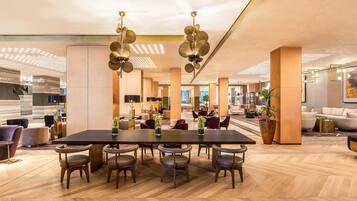 A spacious lobby with a large wooden table, comfortable seating, and modern lighting fixtures.