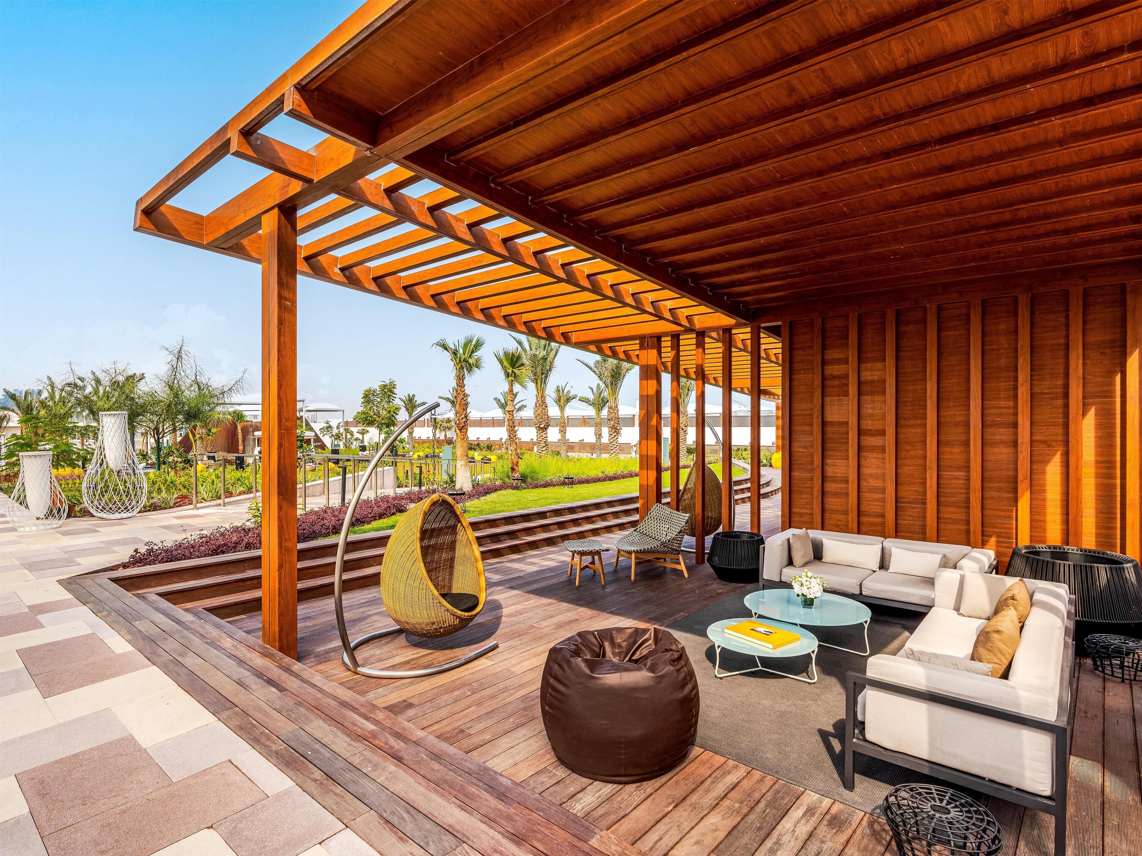Un patio exterior con una pérgola de madera, zona de estar y vistas a un jardín ajardinado.