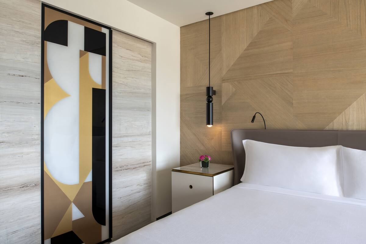 Una habitación de hotel moderna con una cama, una mesita de noche y una lámpara fijada a la pared.