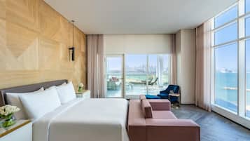 A modern hotel room with a large bed, a seating area with a sofa and armchairs, and a balcony with a city view.