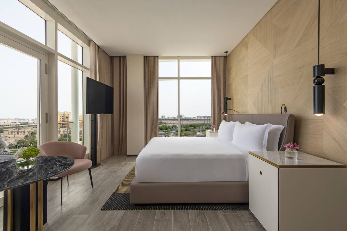 Habitación de hotel moderna con una cama grande, televisión de pantalla plana, escritorio y vistas a la ciudad.