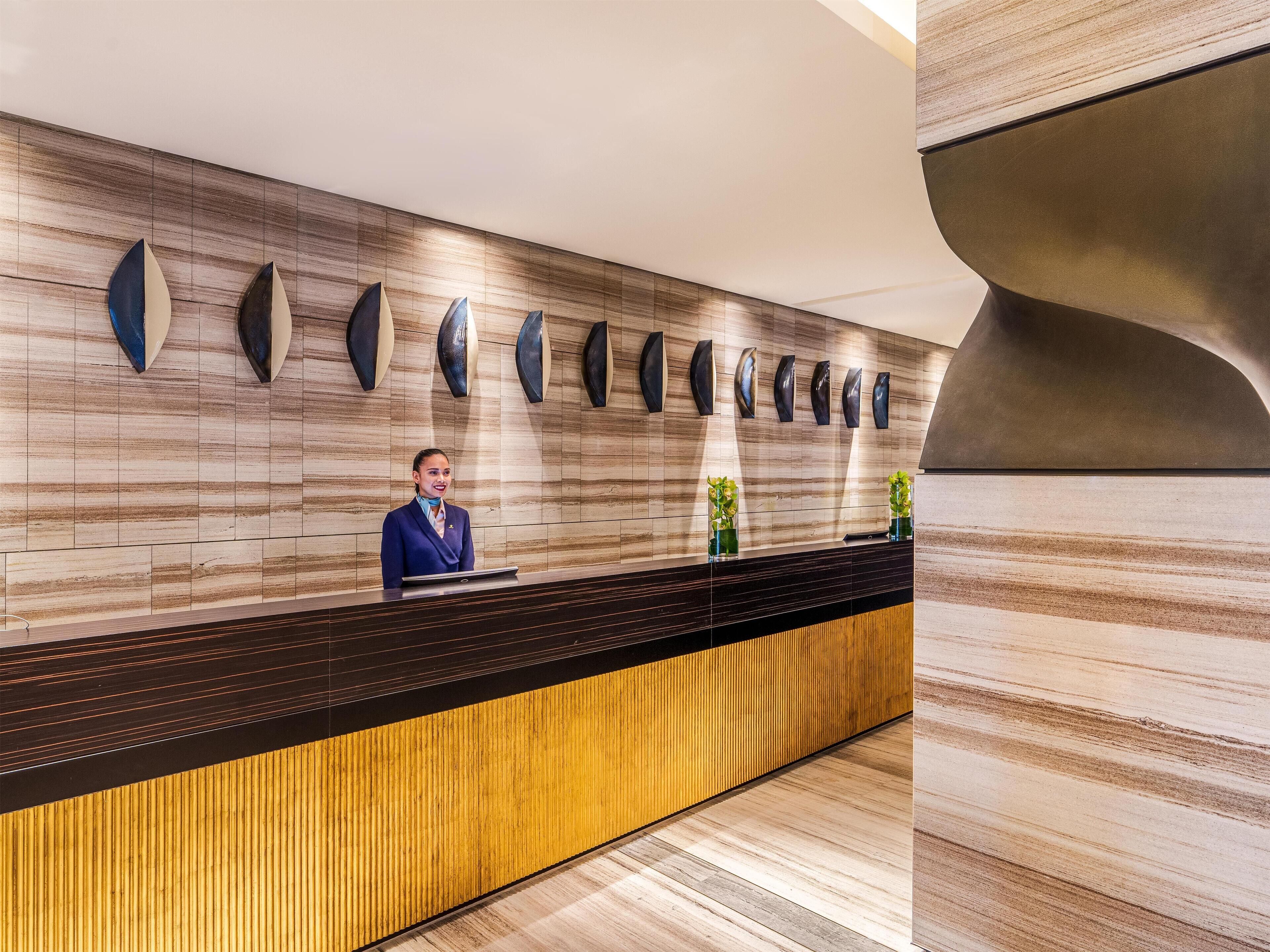 Un mostrador de recepción con un panel de madera, una recepcionista y decoración en la pared.