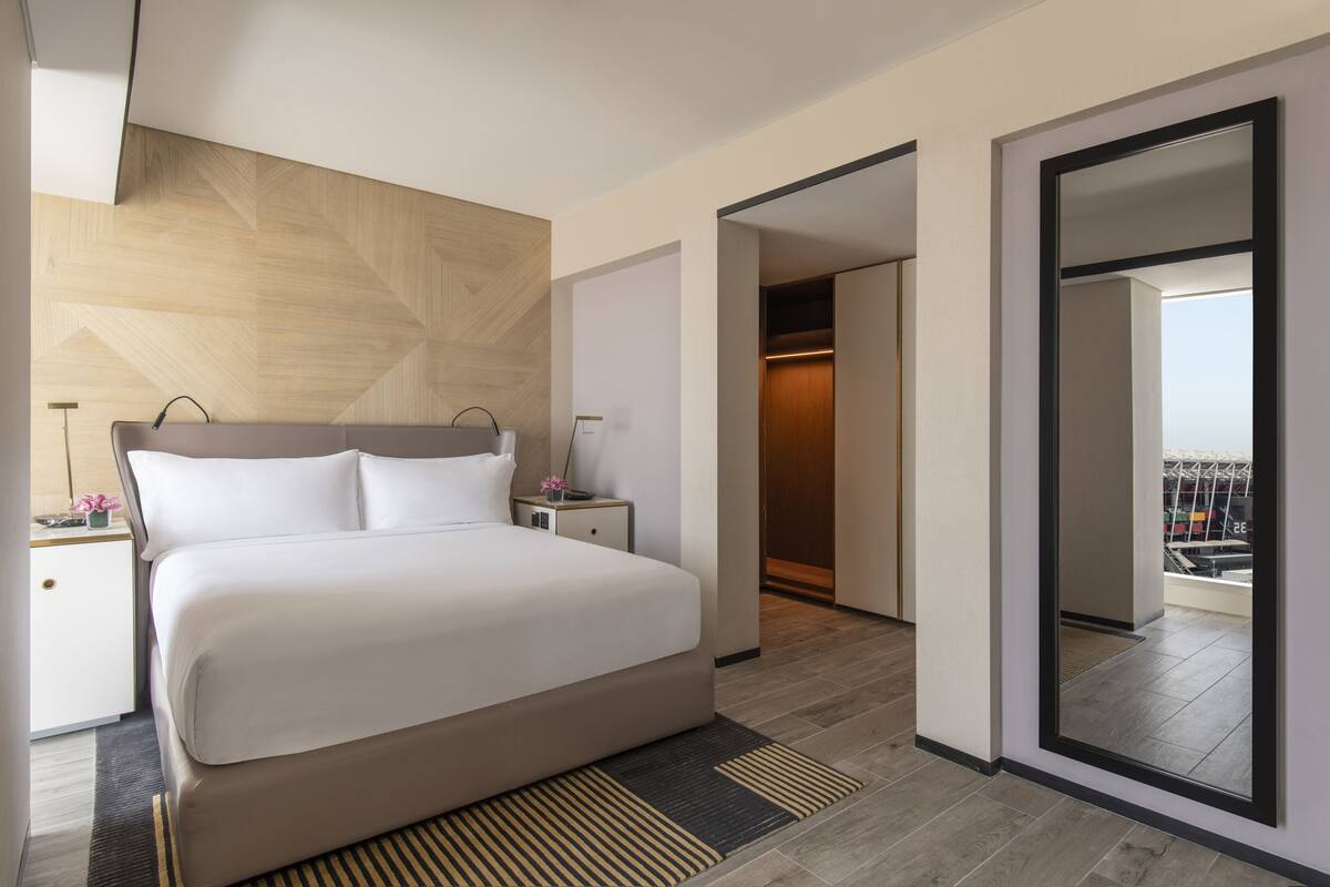 Un hotel moderno con una cama grande, una mesita de noche, un espejo y vistas a la ciudad a través de un amplio ventanal.