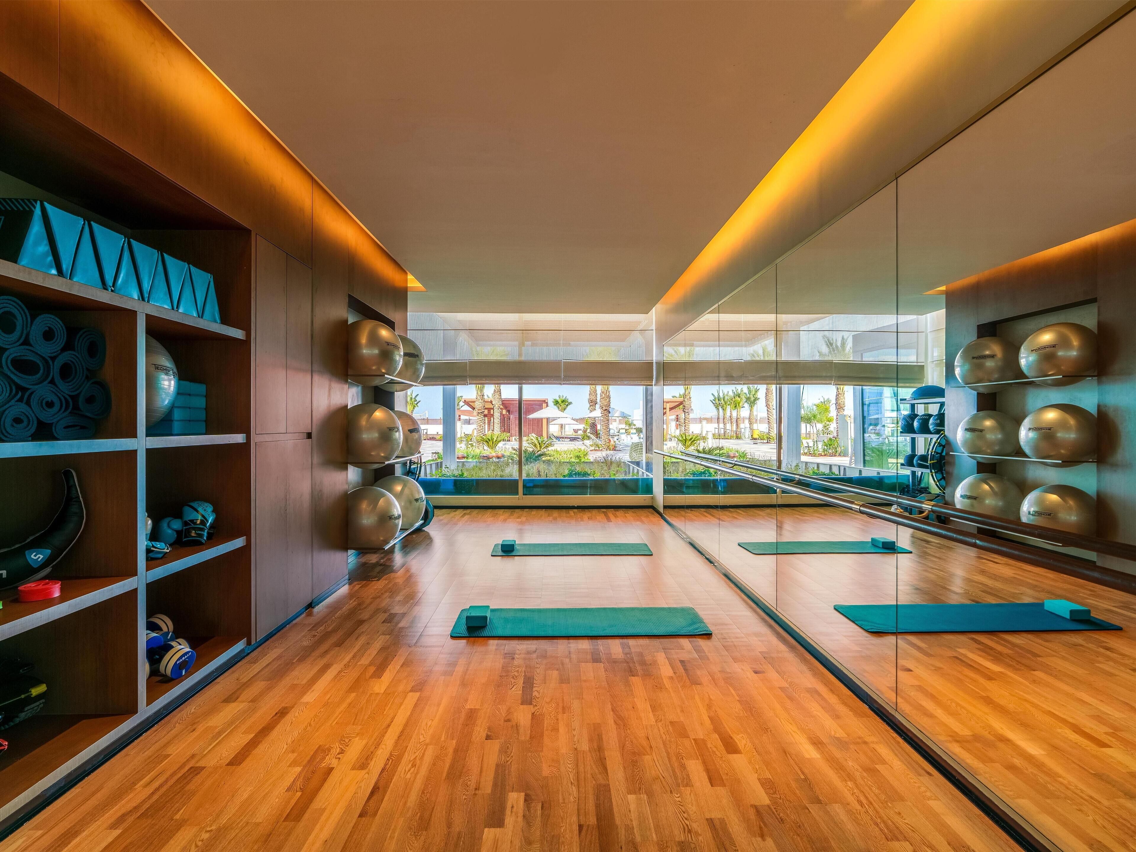 A modern gym with wooden floors, exercise equipment, and large mirrors.