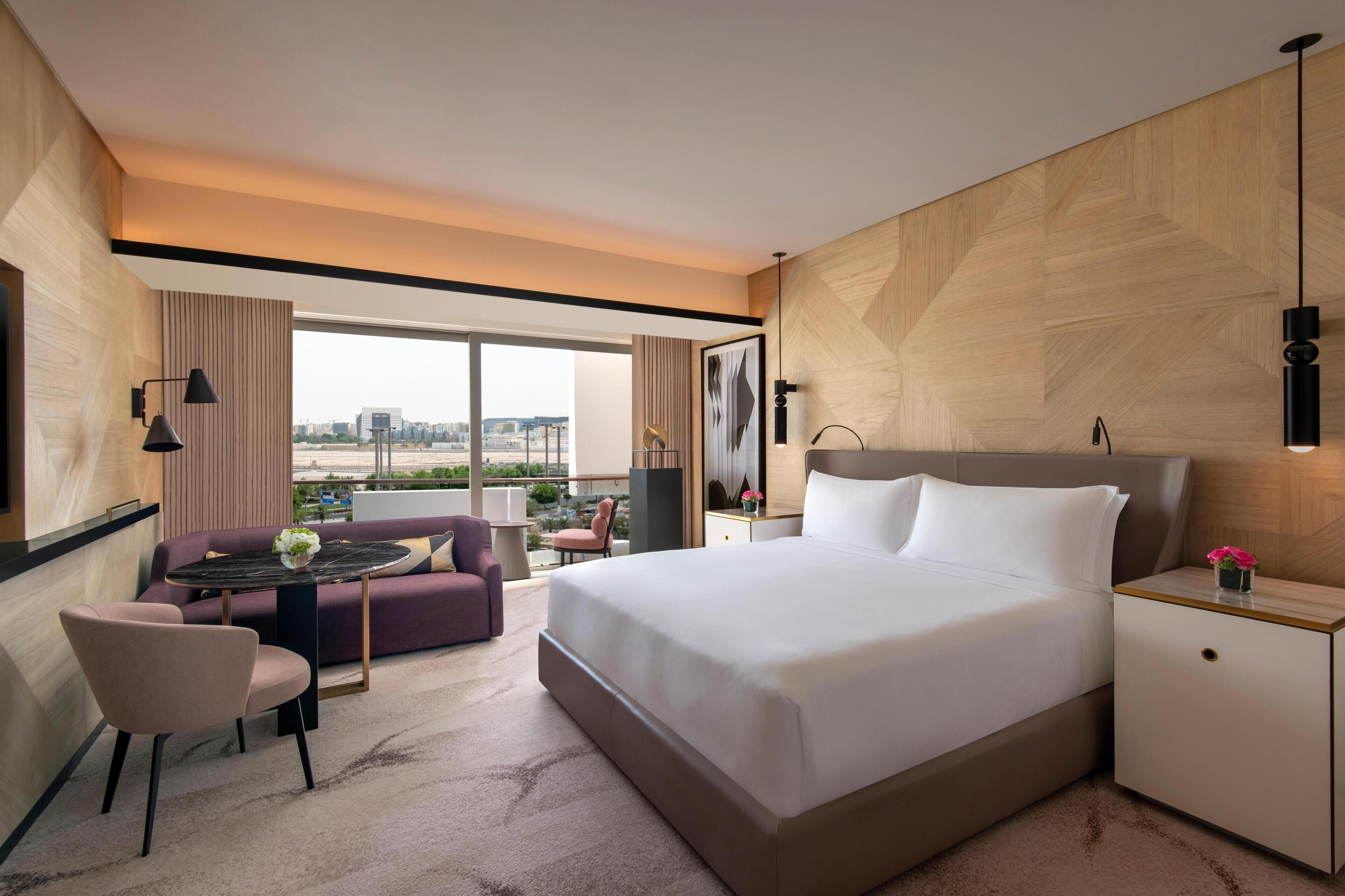 Una habitación de hotel moderna con una cama grande, un sofá, una mesita y vistas a la ciudad.