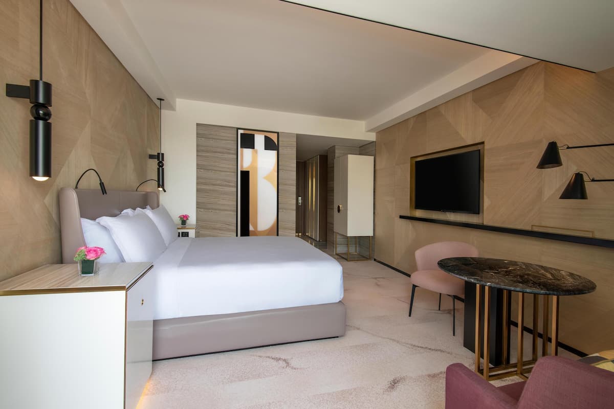 Una habitación de hotel moderna con una cama grande, un escritorio, una mesa redonda, un televisor y una silla.