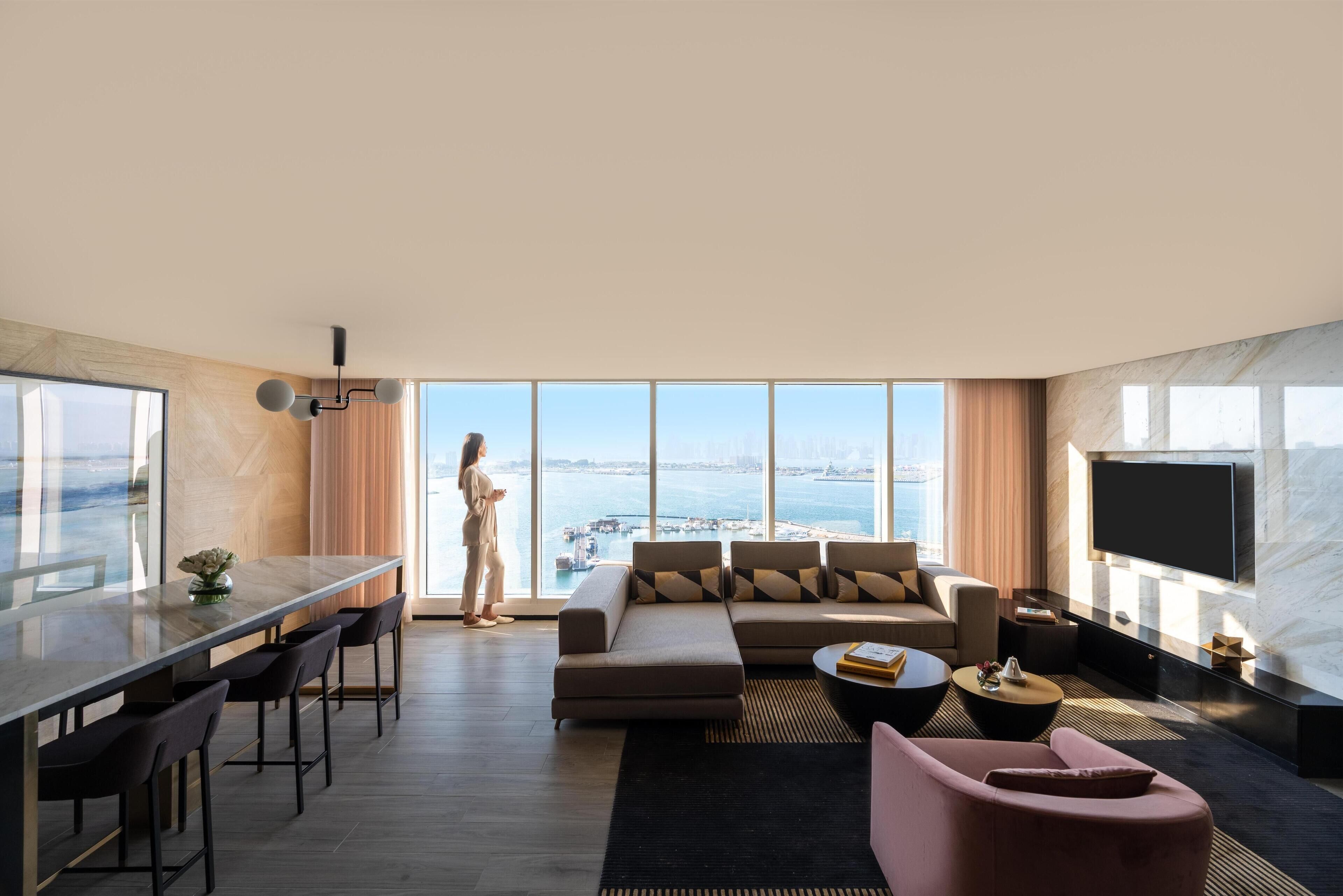 A modern living room with a large window, a sofa, a coffee table, and a TV mounted on the wall.