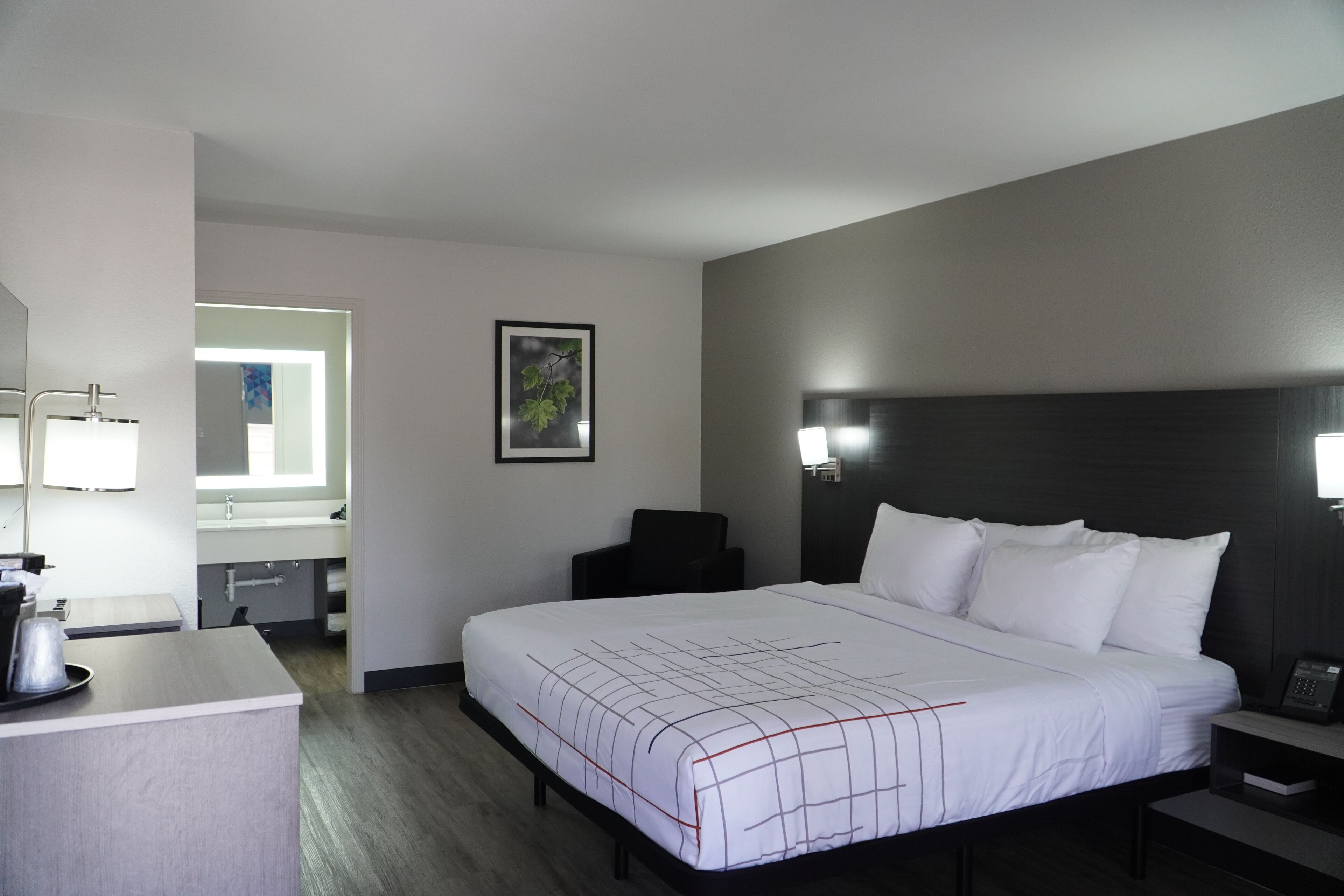 Habitación de hotel con una cama grande, mesitas de noche, un escritorio con una silla, un espejo y un cuadro en la pared.