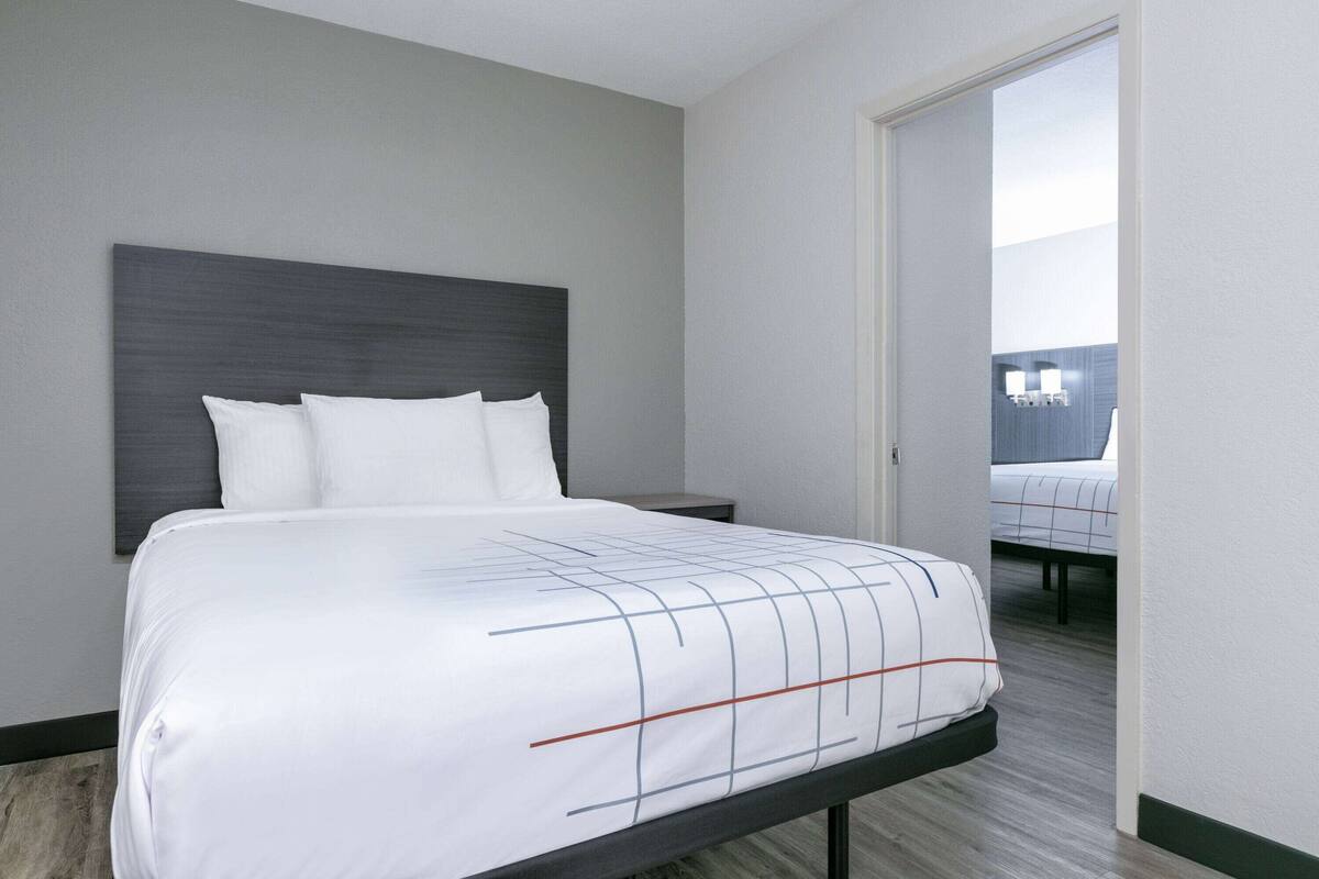 A neatly made bed with a white and grey striped bedspread, a dark headboard, and a wooden floor.