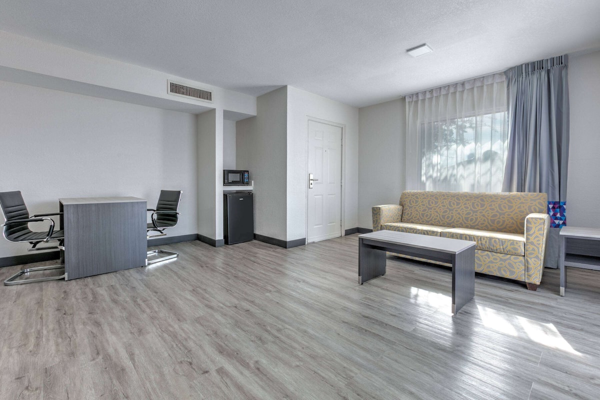 A modern living room with a sofa, a coffee table, and two chairs. There is a small kitchenette with a microwave and a refrigerator.