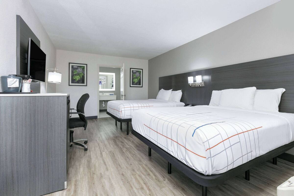 A hotel room with two beds, a desk with a chair, a TV, and a mirror.