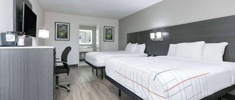 A hotel room with two beds, a desk with a chair, a TV, and a mirror.