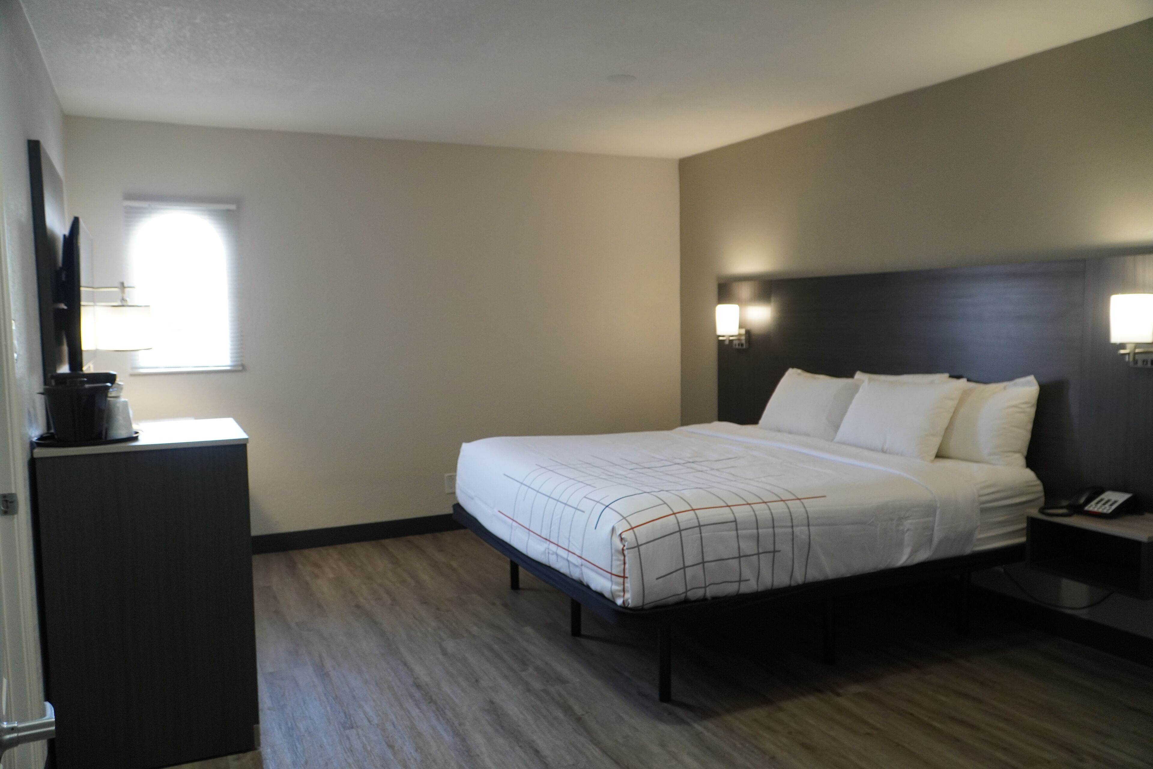 Una habitación de hotel con cama, mesita de noche, lámpara y un pequeño escritorio con teléfono.