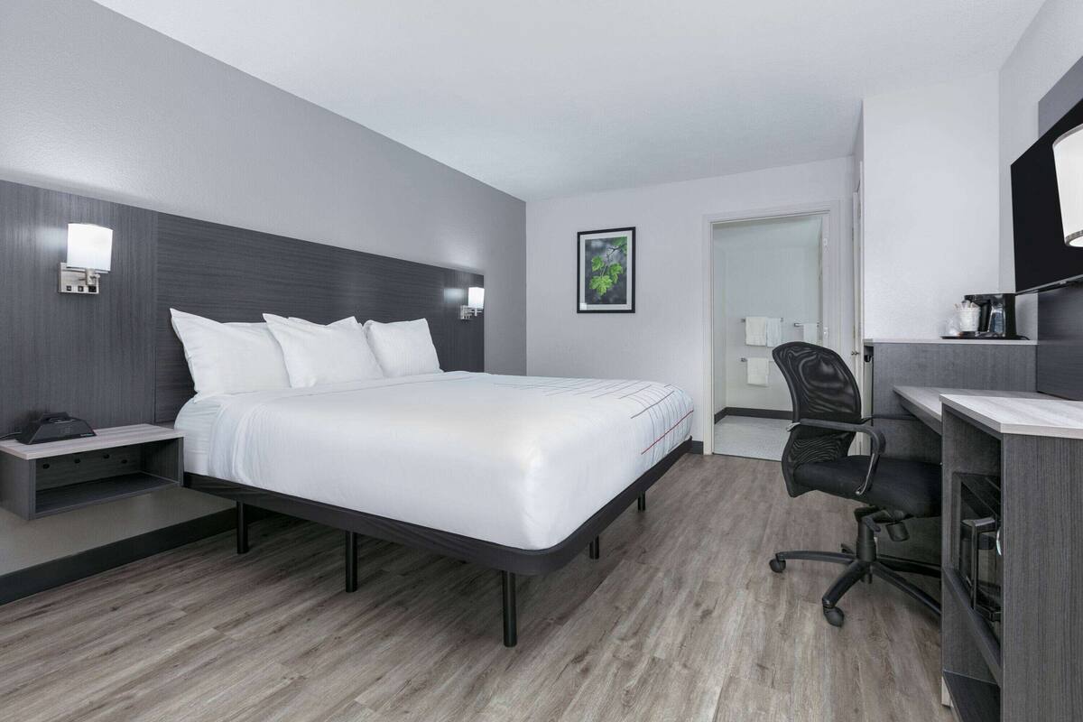 A modern hotel room with a large bed, bedside tables, a desk with a chair, and a mirror.