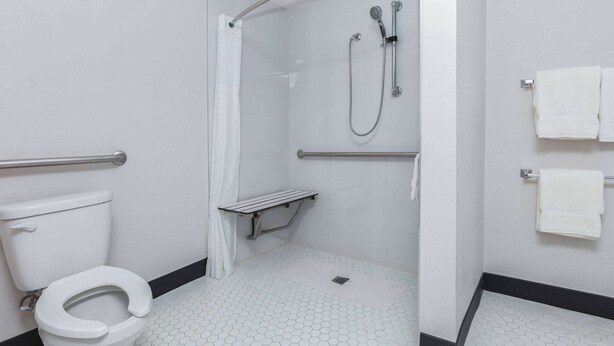 A bathroom with a white toilet, a shower with a glass door, and a towel rack with two towels. - La Quinta Inn by Wyndham Dallas Uptown (Dallas)