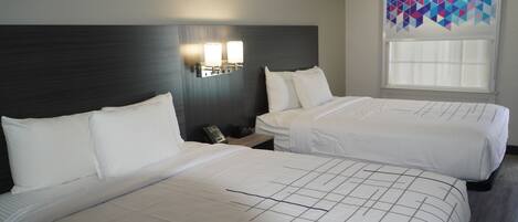 A hotel room with two beds, a nightstand with a phone, and a window with a geometric curtain.