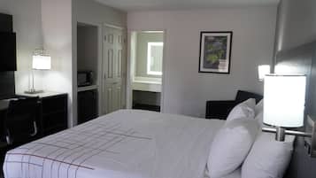 Quarto de hotel com uma cama grande, uma escrivaninha com cadeira, televisão e uma pequena cozinha.