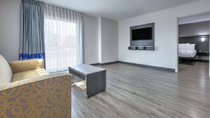 Ein modernes Hotelzimmer mit einer Couch, einem flachbildfernseher an der Wand und einem Bett mit Kopfteil.