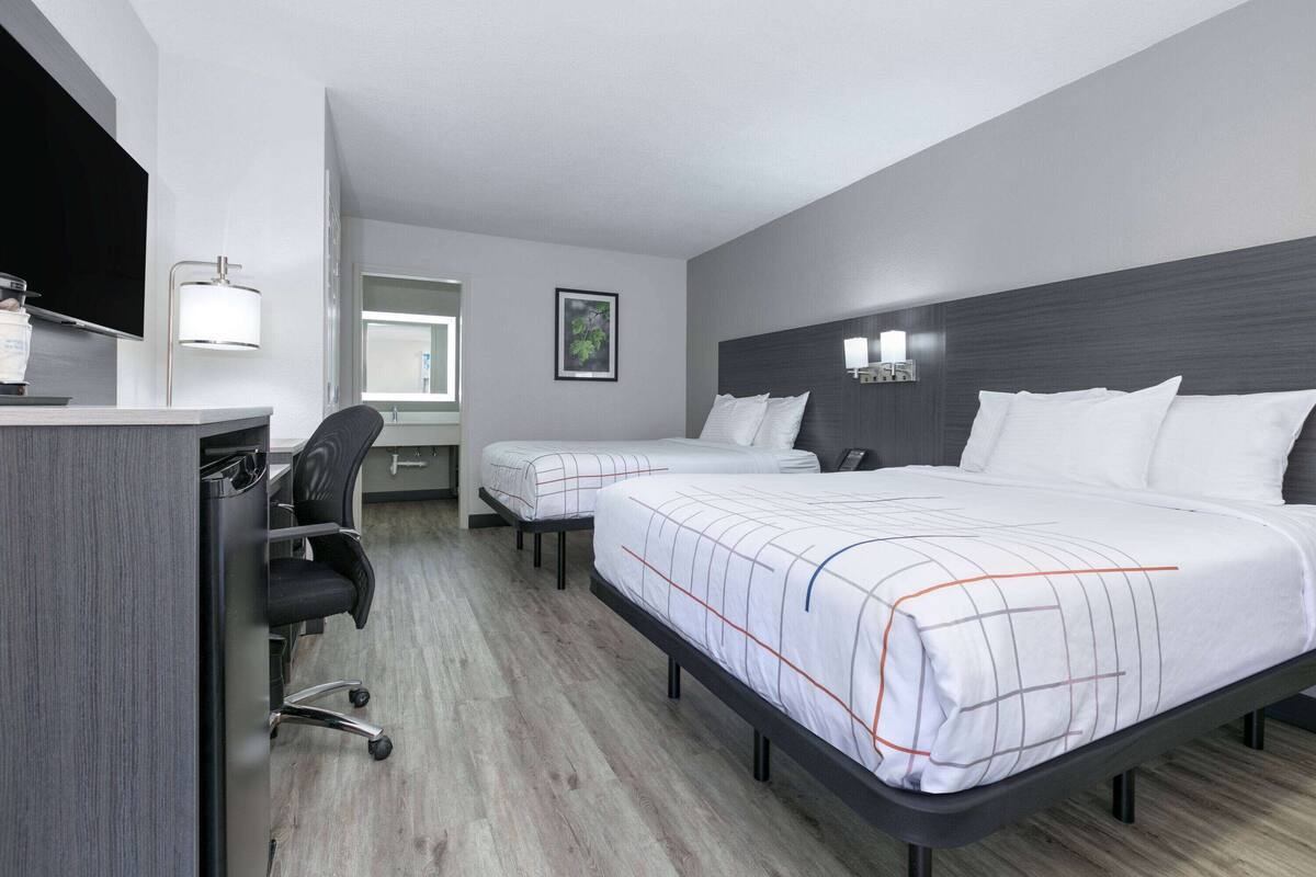 Ett hotellrum med två sängar, ett skrivbord, en stol, en TV och ett fönster.