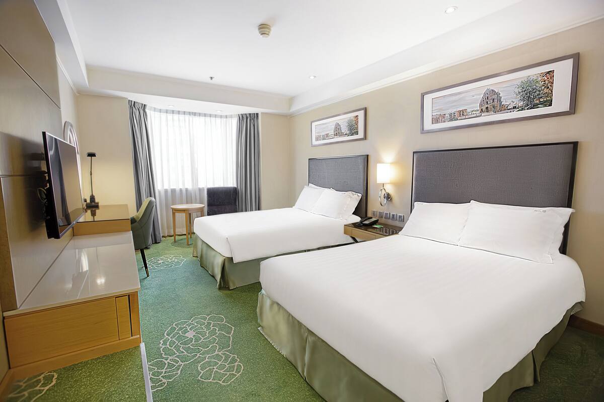 A hotel room with two beds, a desk, a chair, and a television.