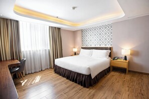 A hotel room with a large bed, bedside tables with lamps, a desk, and a chair.