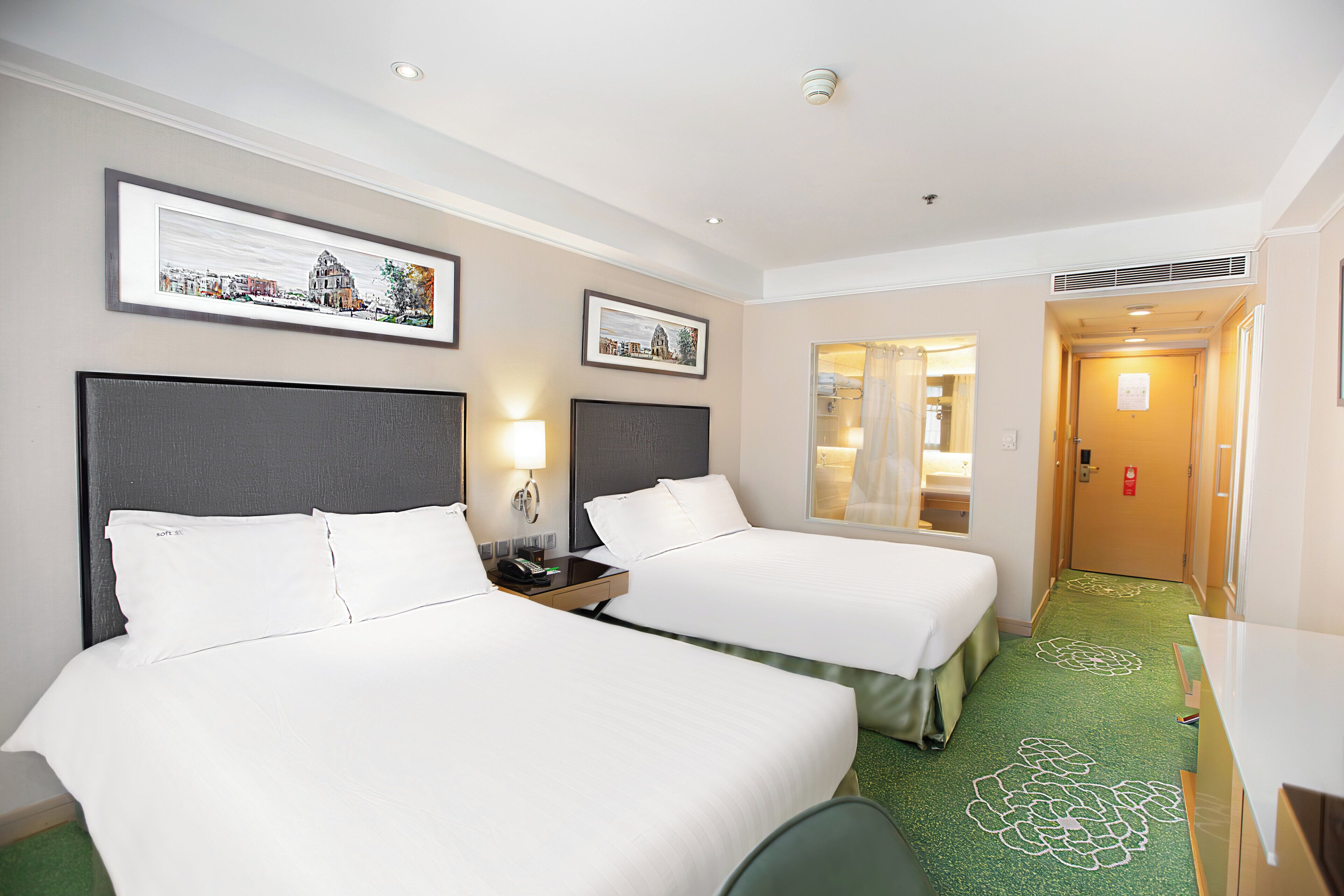A hotel room with two beds, a desk, and a bathroom visible through an open door.