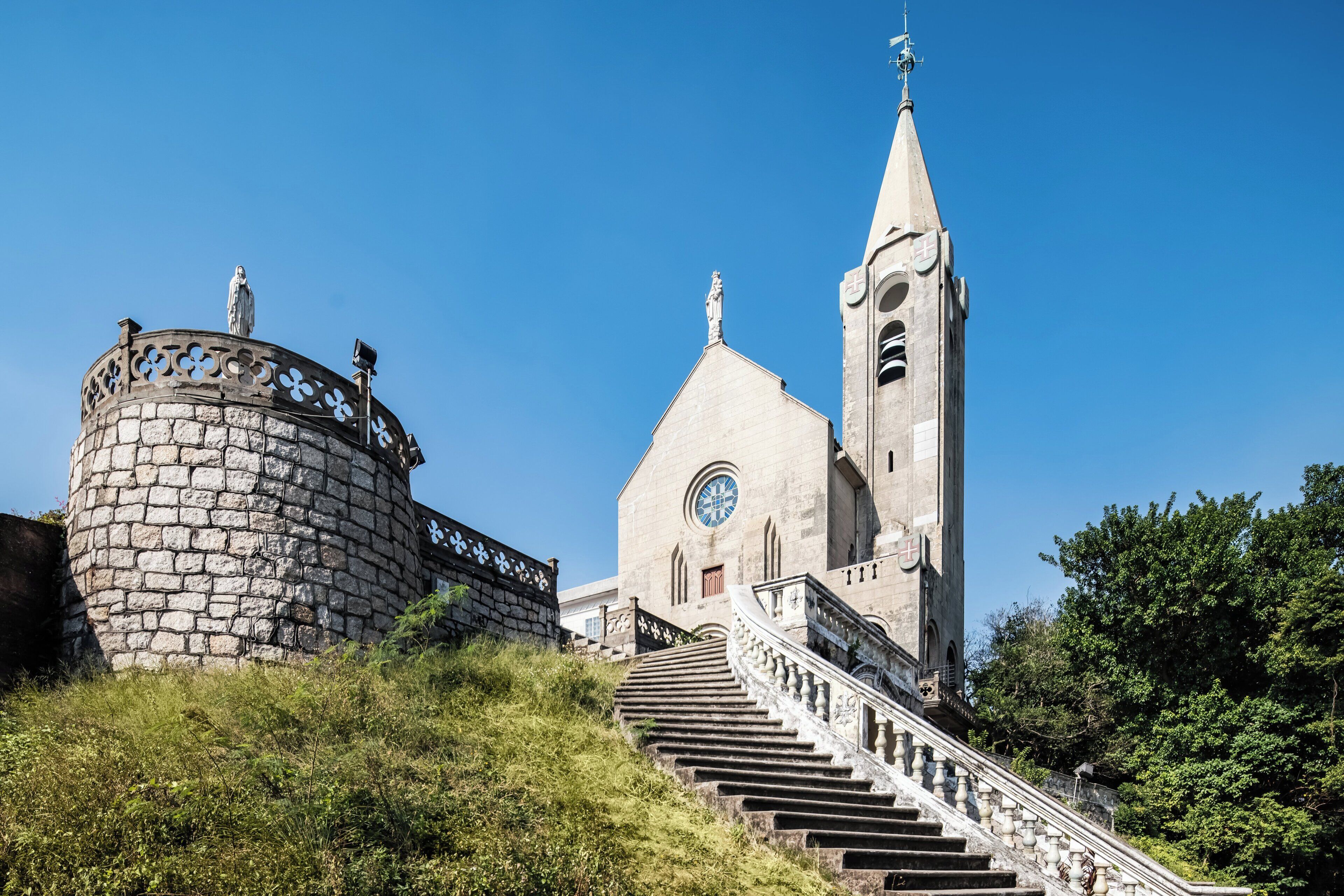 A historic church with a tall bell tower and a round stone tower with statues on top.