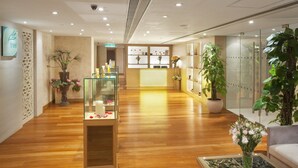 A modern hotel lobby with wooden flooring, a reception desk, a glass display case, and potted plants. - Holiday Inn Macau by IHG (Macau)