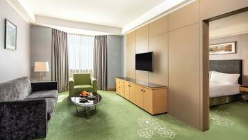 A hotel room with a green carpet, a sofa, a chair, a small table, a TV, a bed, and a wardrobe.