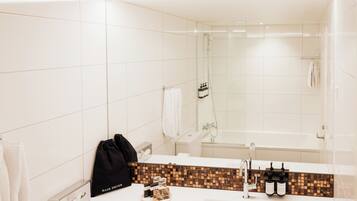 A modern bathroom with a large mirror, a white sink, a shower, and a towel rack.