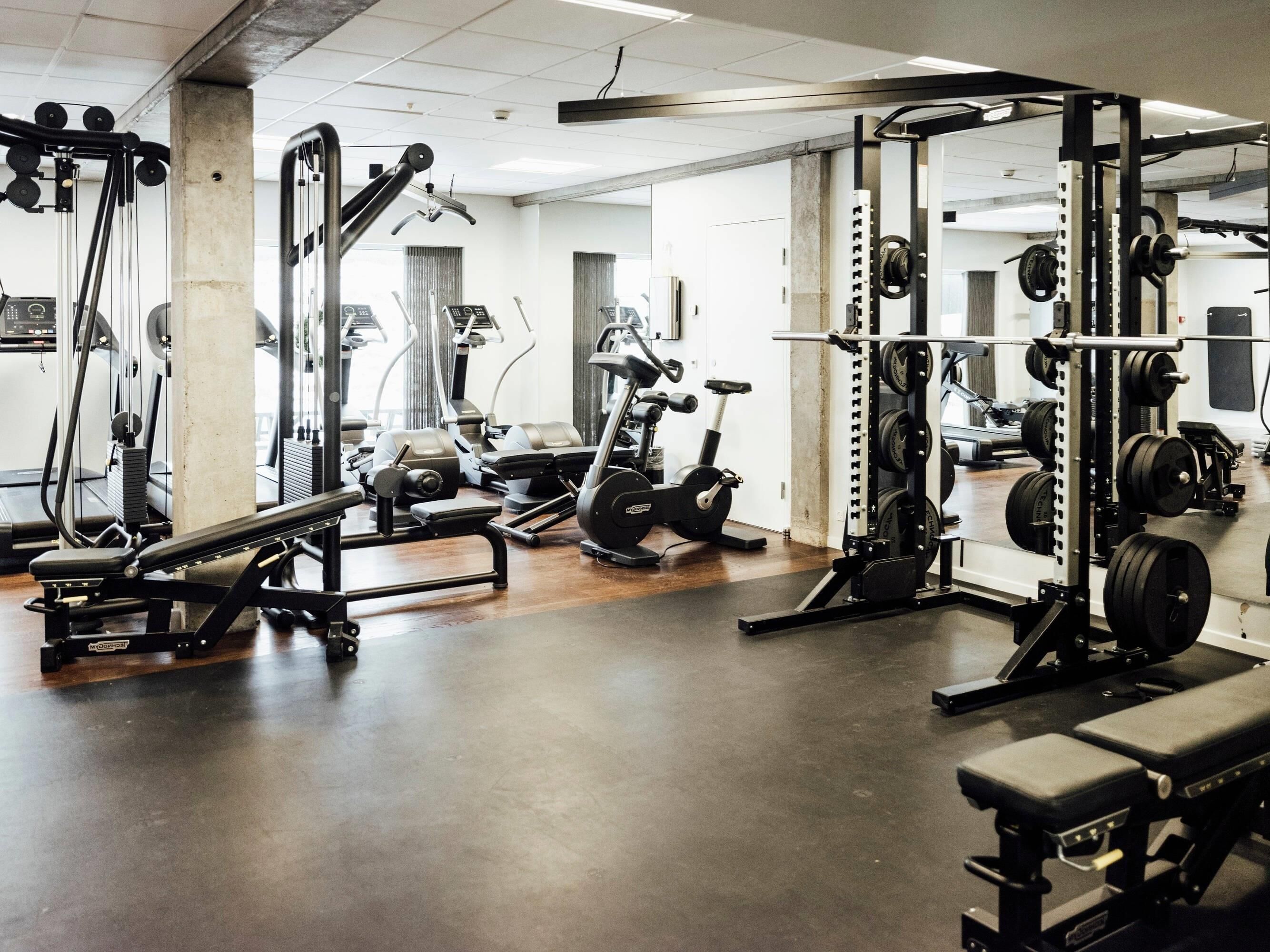 Una palestra con diverse attrezzature per esercizi, tra cui una panca piana, rastrelliere per pesi e macchinari cardio.