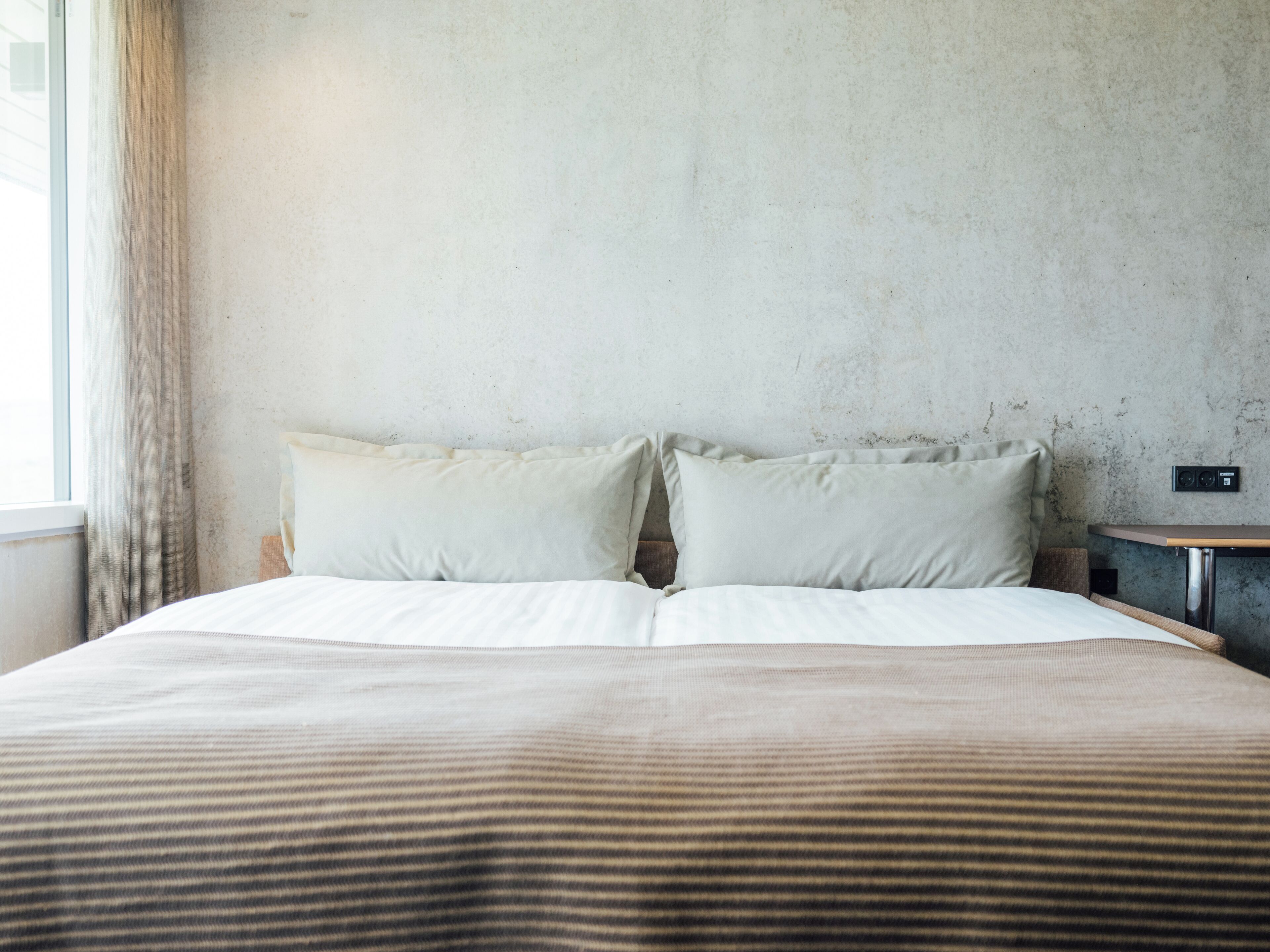 A bed with two pillows, a wooden headboard, and a nightstand with a lamp.