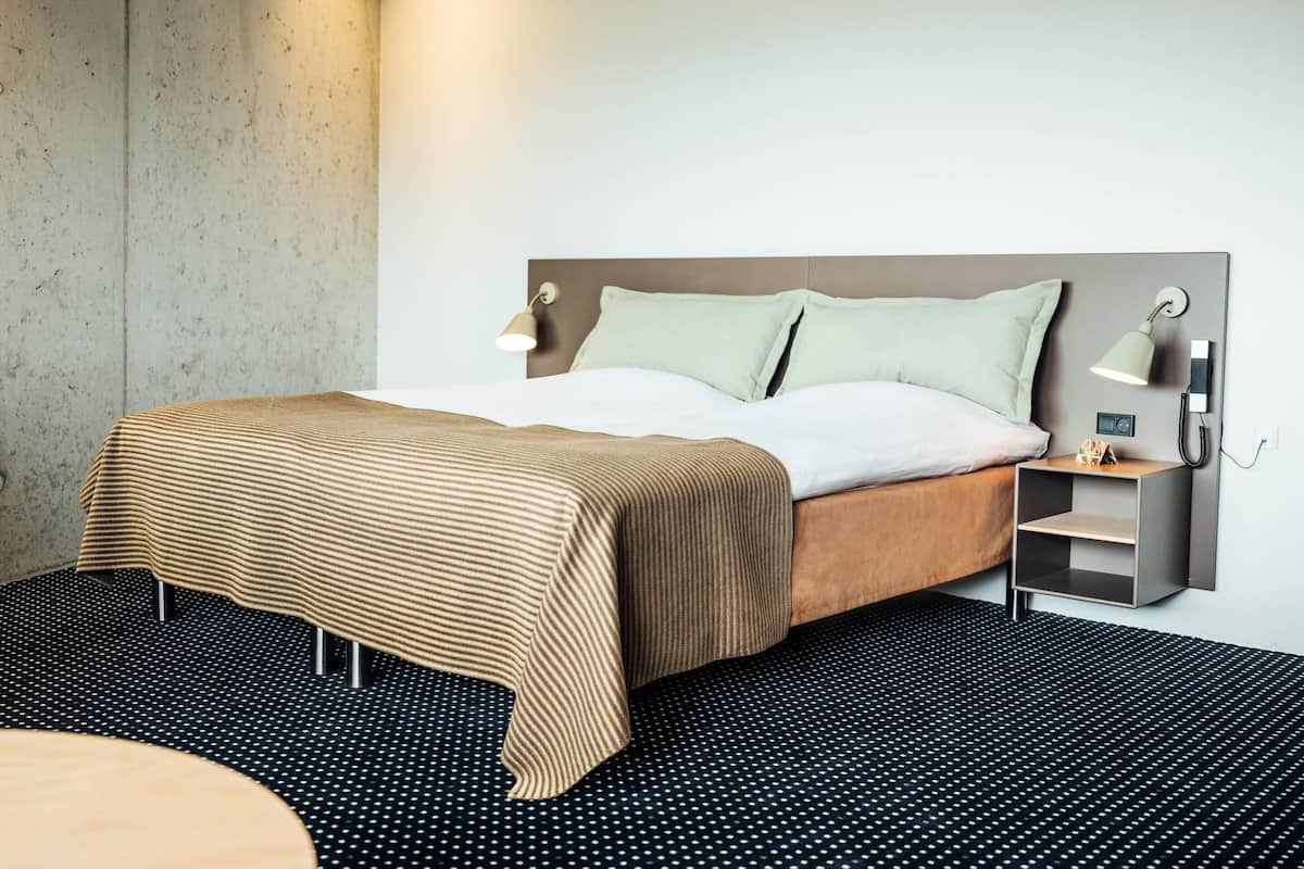 Une chambre d’hôtel moderne avec un grand lit, une table de chevet avec une lampe et un téléphone fixé au mur.