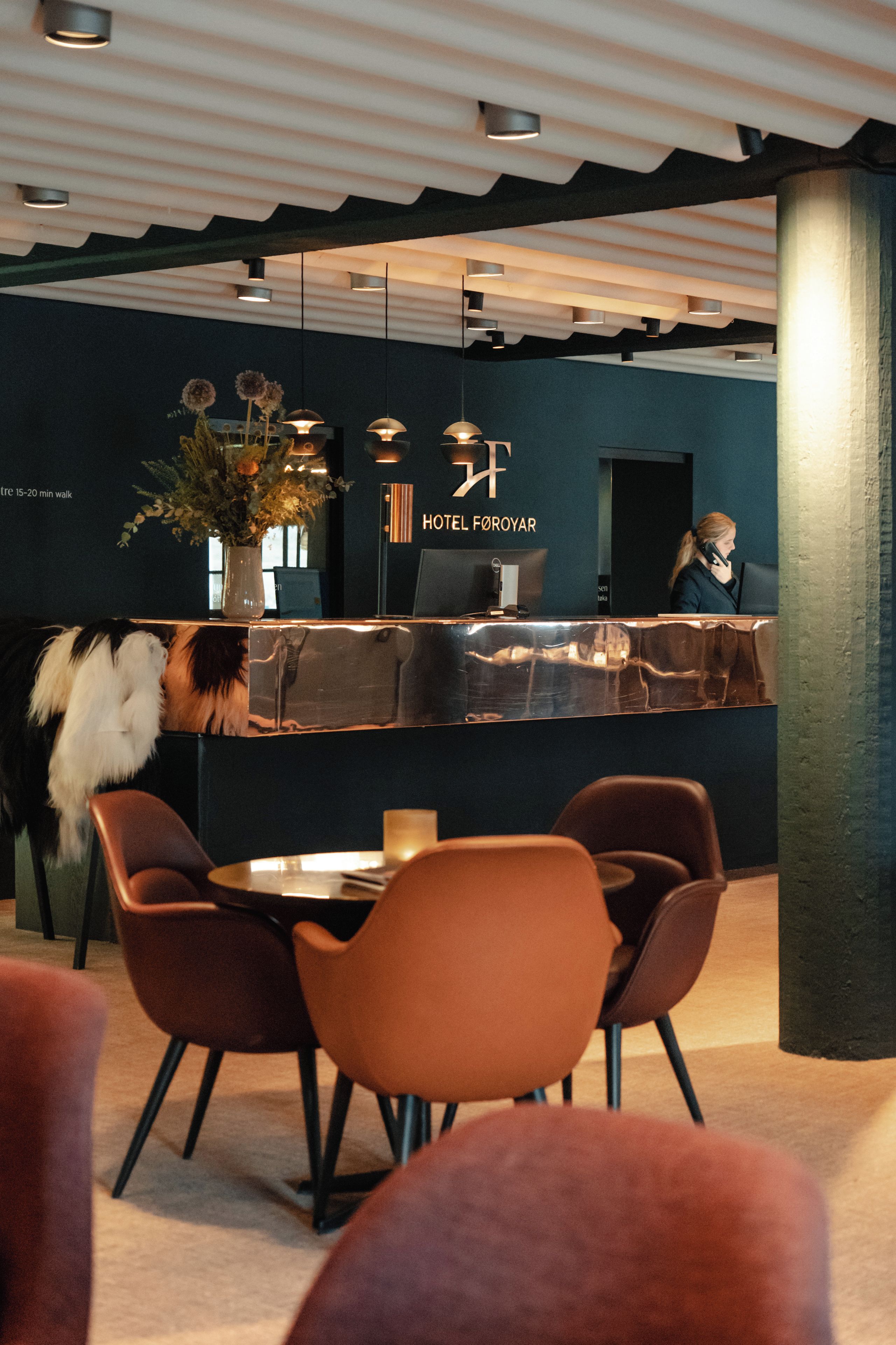 Un espace d’accueil d’hôtel au design moderne, comprenant un comptoir d’accueil, des chaises et une plante décorative.