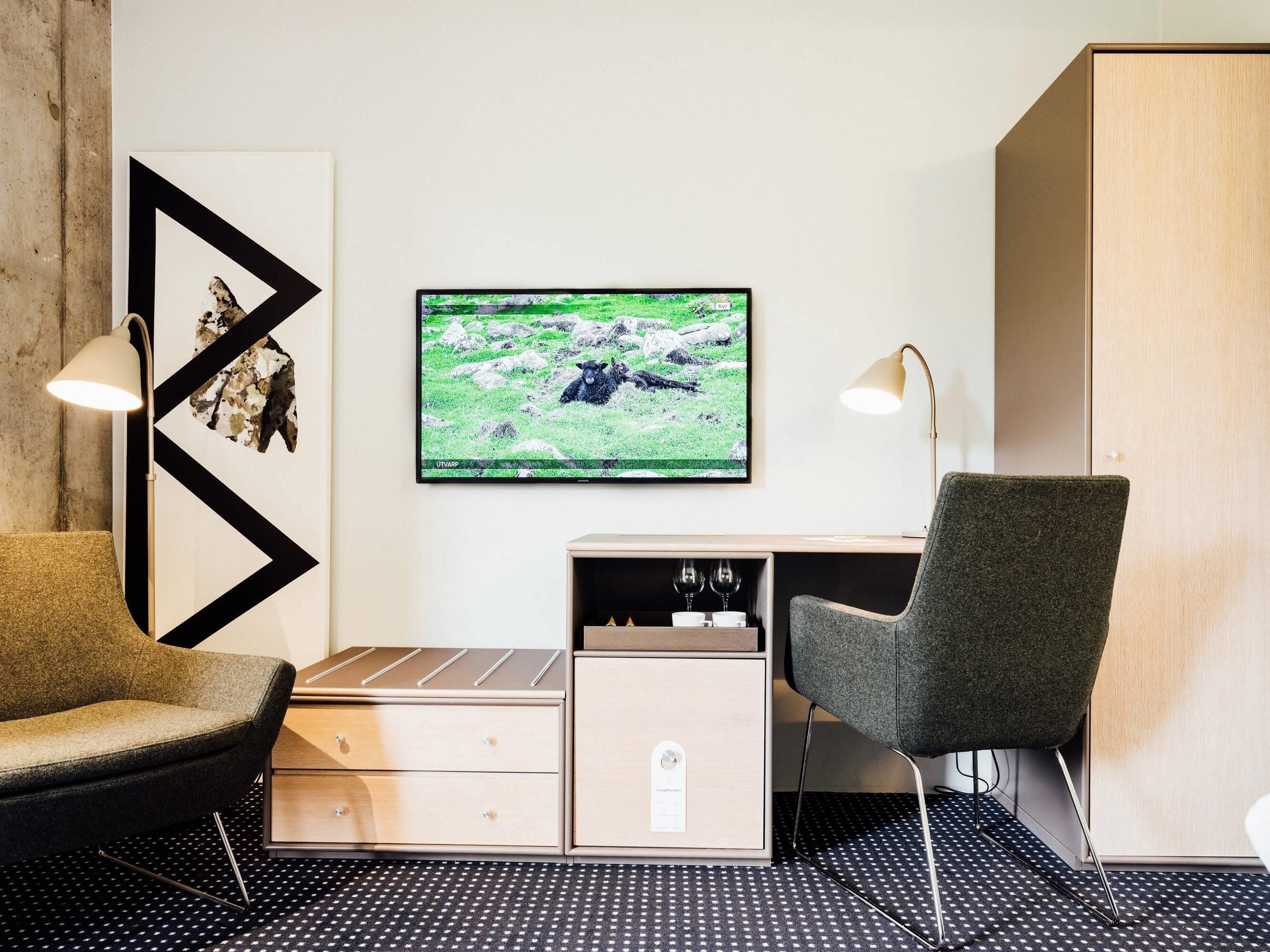 Ein modernes Hotelzimmer mit einer Couch, einem Schreibtisch, einem Sessel, einem Fernseher und einem Schrank.