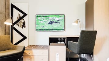 Ein modernes Hotelzimmer mit einer Couch, einem Schreibtisch, einem Sessel, einem Fernseher und einem Schrank.