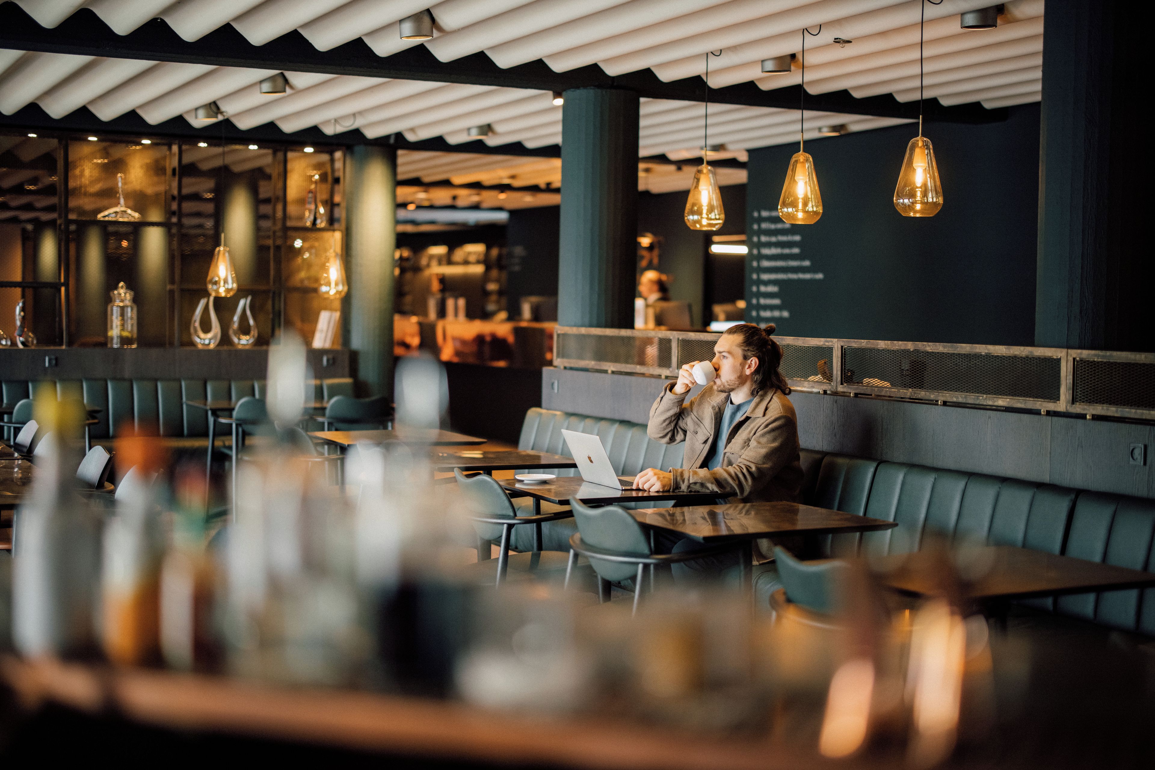 Una persona sentada a una mesa con una computadora portátil, en un restaurante con lámparas colgantes y un diseño de interiores moderno.
