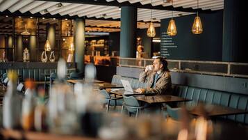 Una persona sentada a una mesa con una computadora portátil, en un restaurante con lámparas colgantes y un diseño de interiores moderno.