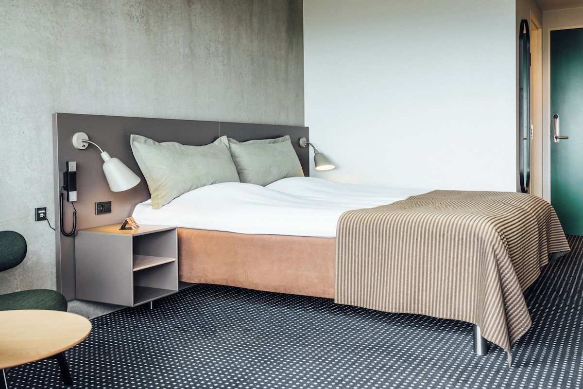 Una habitación de hotel con una cama, lámparas de noche, un escritorio y una silla.