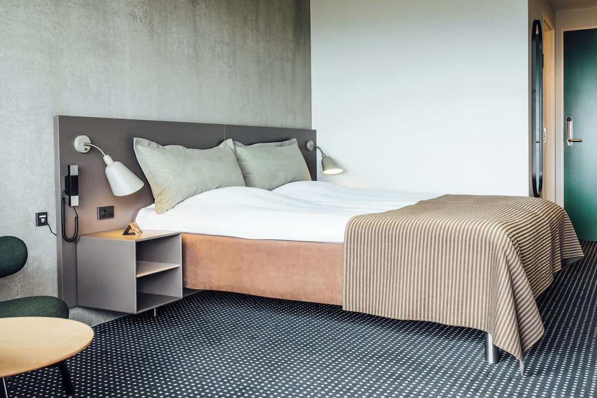 Une chambre d’hôtel avec un lit, des lampes de chevet, un bureau et une chaise.