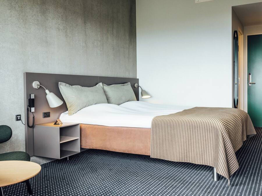 Une chambre d’hôtel avec un lit, des lampes de chevet, un bureau et une chaise.