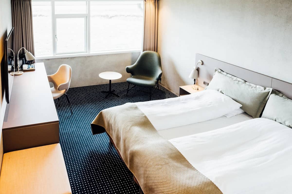 Une chambre d’hôtel avec un lit, un bureau, une chaise, une petite table et une fenêtre avec des rideaux.