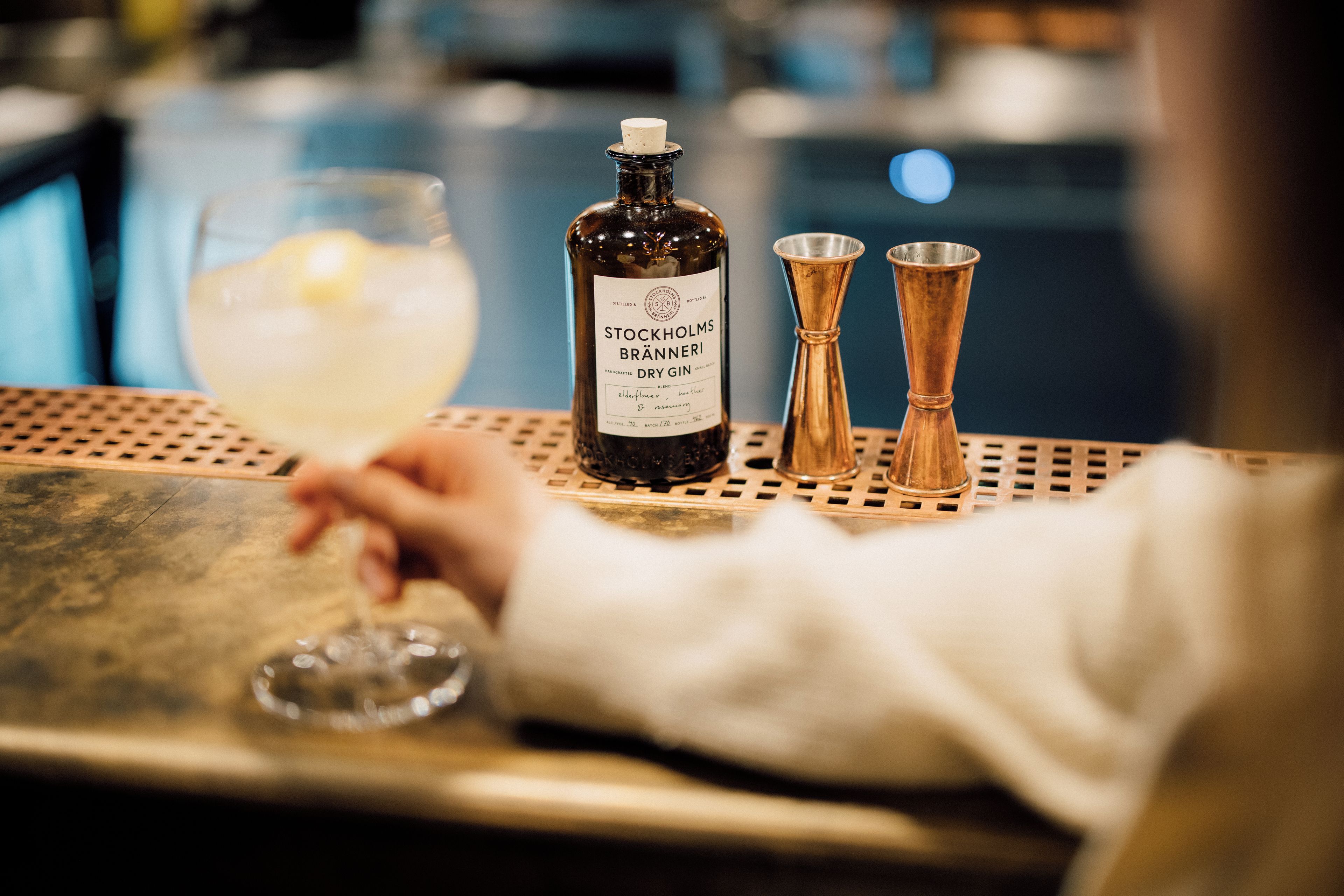 Un bar con una botella de ginebra seca Stockholms Branneri, un vaso con una rodaja de limón y dos vasos medidores de cobre.