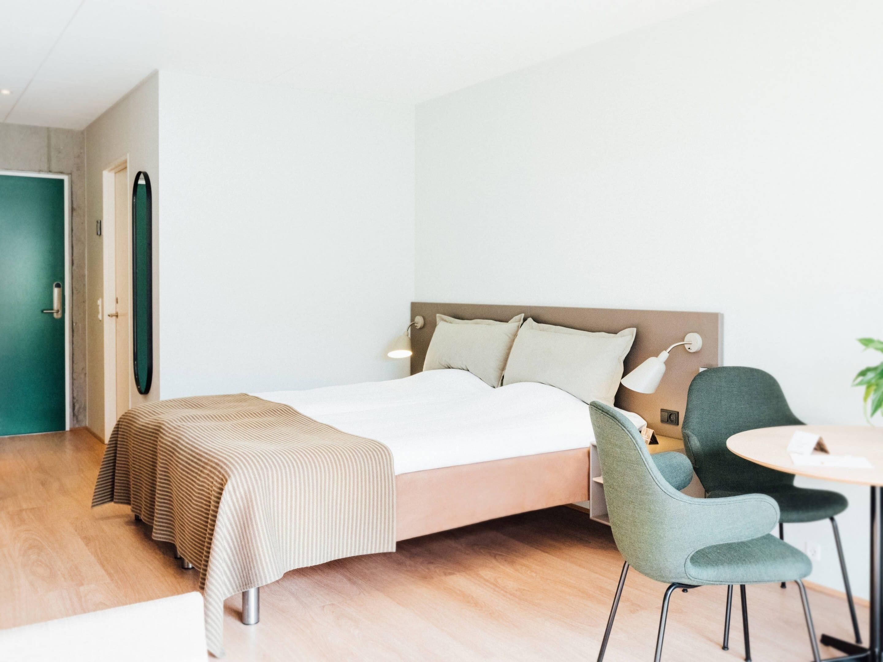 A modern hotel room with a bed, a desk, and a chair.