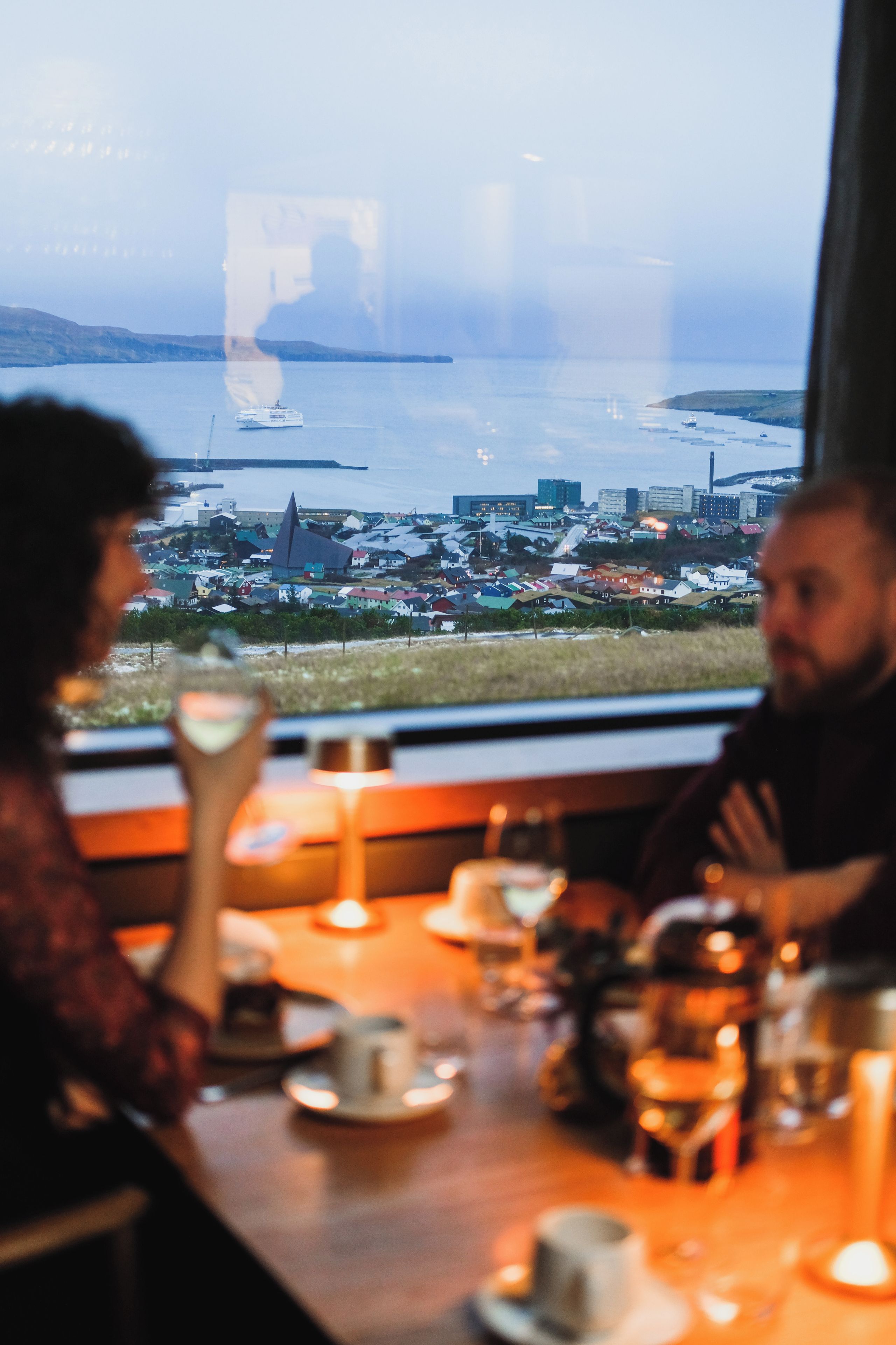 A dining area with a view of a coastal town and a ship.